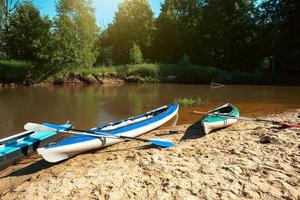 Tourist canoes with paddles stand on the river coast in summer on a water hike. Rafting on inflatable and frame double and triple kayak boats, family trip, extreme adventure in summer photo