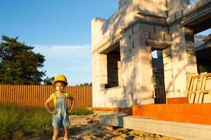 una niña pequeña con un casco amarillo está jugando al constructor en el sitio de construcción de su futuro hogar. sueña con mudarse, elegir una profesión, la educación de los niños. foto