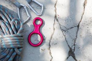 Coiled climbing rope and steel carabiner. Mountain climbing equipment harness, brakes, quickdraws, self-insurance, belay device eight. On a stone background with cracks. Flatlay, copy space photo