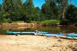 Tourist canoes with paddles stand on the river coast in summer on a water hike. Rafting on inflatable and frame double and triple kayak boats, family trip, extreme adventure in summer photo