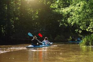 Family kayak trip. Man and woman and elderly couple senior and seniora rowing boat on the river, a water hike, a summer adventure. Eco-friendly and extreme tourism, active and healthy lifestyle photo