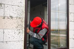 The window installer adjusts the hinges and checks new windows in the cottage under construction. Ordering windows with golden layout and brown lamination for a private house. A worker in uniform photo