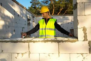 Construction worker at construction site measures the length of the window opening and the wall with tape measure. Cottage are made of porous concrete blocks, protective clothing - hardhat and a vest photo