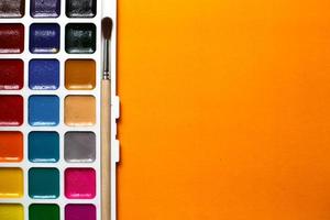 A palette of watercolors and paintbrushes on an orange background photo