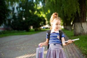 una niña de apariencia caucásica con uniforme escolar con una mochila y el libro y un juego de marcadores. De vuelta a la escuela. primaria, desarrollando actividades para preescolares. espacio para texto foto