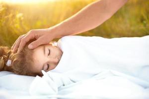 Girl sleeps on white bed in the grass, fresh air. Dad's hand gently pats his head. Eco-friendly lifestyle, healthy sleep, benefits of ventilation, hardening, clean nature, ecology, children's health photo