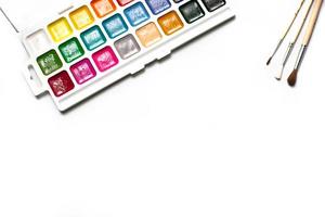 A palette of eighteen-color watercolors and paintbrushes on a white background with space for text. photo