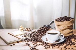 taza de café y granos de café tostados en una bolsa de papel sobre un fondo borroso foto