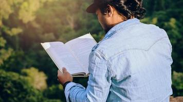 el hombre asiático viaja relájese en las vacaciones. los asientos se relajan y leen libros sobre acantilados rocosos. en la montaña de verano foto