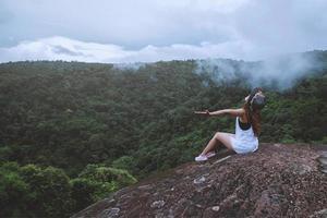 Asian woman travel nature. Travel relax. Freedom happy traveler woman standing with raised arms and enjoying a beautiful nature on peak of foggy mountain. photo