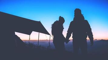 amante mujer y hombre asiáticos viajan relajarse acampando en las vacaciones. en la montaña estar de pie ver salir el sol. tailandia foto