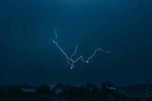 Lightning in sky over city. Bright flashes on dark night. Thunderclouds and electricity discharges in  atmosphere. photo