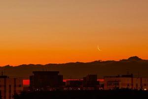 Waning moon in colorful sky. Satellite of Earth over  city in rays of sun. photo
