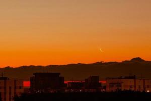 luna menguante en el cielo colorido. satélite de la tierra sobre la ciudad en rayos de sol. foto