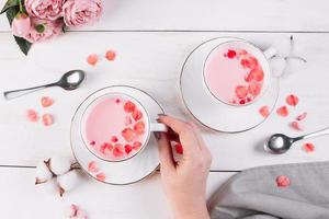 Pink matcha with rose petals on white background. Female hand holds a cup with trending vegan tea. Relaxing drink in the sleepy time. photo