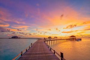 Sunset on Maldives island, luxury water villas resort and wooden pier. Beautiful sky and clouds and beach background for summer vacation holiday and travel concept photo