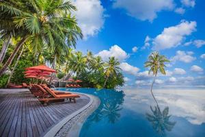 Panoramic holiday landscape. Luxurious beach resort hotel swimming pool and beach chairs or loungers under umbrellas with palm trees, blue sunny sky. Summer island seaside, travel vacation background photo