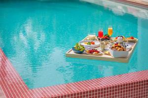 desayuno en piscina, desayuno flotante en lujoso resort tropical. mesa para relajarse en el agua tranquila de la piscina, desayuno saludable y plato de frutas junto a la piscina del centro turístico. pareja tropical playa estilo de vida de lujo foto