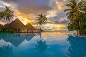 puesta de sol de lujo sobre la piscina infinita en un complejo hotelero de verano frente a la playa en un paisaje tropical. tranquilo estado de ánimo de fondo de vacaciones de vacaciones de playa. increíble vista de la playa de la puesta del sol de la isla, piscina de palmeras foto