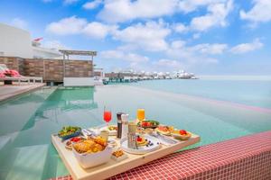 Breakfast in swimming pool, floating breakfast in tropical resort. Table relaxing in calm pool water, healthy breakfast and fruit plate by resort pool. Exotic summer diet. Tropical beach lifestyle photo