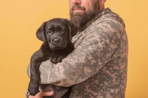 hombre vestido con ropa militar con un cachorro labrador retriever en sus brazos. hombre y perro. foto