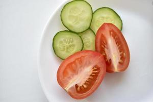 Sliced red tomatoes and green cucumber close-up on a plate photo