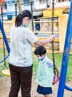 los padres llevan a los estudiantes a las actividades familiares. jugar juegos mecánicos en el patio de recreo, subirse a un columpio, columpiarse ligeramente y divertirse para dos. por la tarde después de la escuela foto