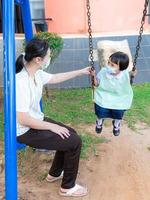 los padres llevan a los estudiantes a las actividades familiares. jugar juegos mecánicos en el patio de recreo, subirse a un columpio, columpiarse ligeramente y divertirse para dos. por la tarde después de la escuela foto