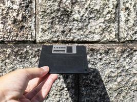 Hand holding a Floppy A disc in an old wall hole. Studying because you don't have a reader. It is an old technology with a square shape. photo