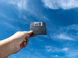 Hand holding a Floppy A disc, insert the reader. to read and write data It's technology old that have been used for a long time has a square shape the background is the sky photo