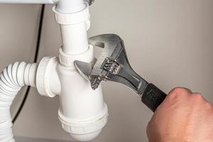 Male plumber fixing sink pipe with adjustable wrench in kitchen photo