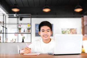 un estudiante asiático feliz usa auriculares y estudia en línea con una videollamada enseñada por un maestro con una tableta inteligente y una computadora portátil desde casa durante el covid-19 foto