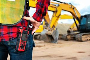 ingeniero civil técnico asiático habla con el equipo por walkie talkie y señala el punto de inspección para el proyecto de trabajo de construcción de transporte con excavadora en el fondo del sitio de ingeniería foto