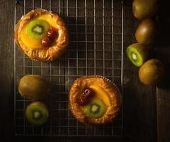 Fruit Tart with Kiwi, Cherry, Persimmon, Put on Steel Strip On the wooden bench With a black background,top view photo