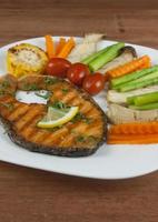 Grilled salmon steak slides until cooked, placed on a white plate with lemon on fish and vegetables, placed around the dish on a wooden floor. photo