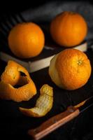 naranjas españolas recién en el libro y pela naranjas antes de comer sobre fondo negro, vista angular foto