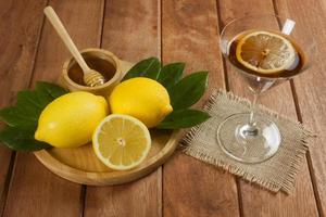 rodajas de limón y té de limón de abeja melífera mezclado con jugo de limón en un vaso de cóctel sobre una mesa de madera foto