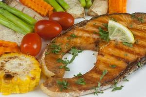 Grilled salmon steak slides until cooked, placed on a white plate with lemon on fish and vegetables, placed around the dish on a wooden floor. photo