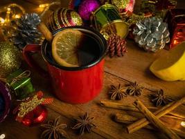 Hot drink alcohol,Mulled red wine in red rustic mugs spices cinnamon stick and citrus fruit.decoratied fir festive on wood table.Celebration christmas and Happy New Year Concept. photo