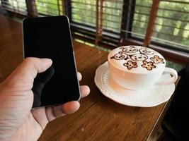 café con leche y un joven hombre de negocios sostienen un teléfono con una pantalla en blanco para publicidad, ingresan un mensaje o un tema de promoción en la cafetería. foto