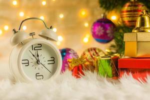 despertador retro de navidad decorado con caja de regalo y abeto festivo sobre fondo borroso bokeh celebración y concepto de feliz año nuevo. foto
