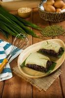 Thai traditional desserts, black sticky rice custard paste in banana leaves on wooden plate photo