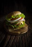 hamburguesa de cerdo casera con tocino a la parrilla contiene verduras, queso, lechuga, cebolla, chile, especias en un plato de madera sobre un suelo de madera. foto