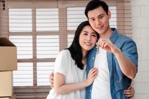 Happy smiling couple in front of the home and holding keys to New Home On Moving In Day, and start a new life family. Concept of homeowner and relocation photo