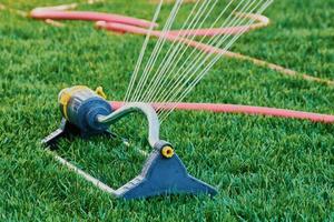 lawn sprinkler is spraying water over the green grass photo