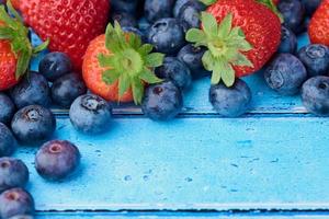 strawberries and blueberries together on a blue wooden background with copy space