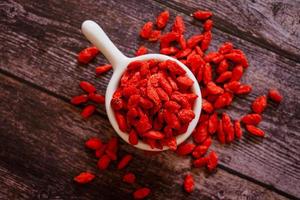 Top view of dried Chinese wolfberries or Goji berry chinese herb or Matrimony vine in the white ceramic bowl isolated on wooden background.  Selected focus. photo