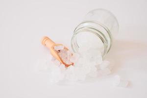 White candy rock sugar or or crystal sugar in wooden scoop and glass jar isolated on white background. White rock sugar is melted and then allowed to crystallize into semi-translucent gemstone. photo