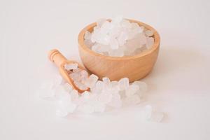 White candy rock sugar or or crystal sugar in wooden scoop and wood bowl isolated on white background. White rock sugar is melted and then allowed to crystallize into semi-translucent gemstone. photo