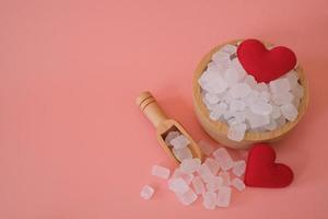 White candy rock sugar, crystal sugar in wooden scoop and glass jar with red heart on pink background. Selected focus. space for text. photo